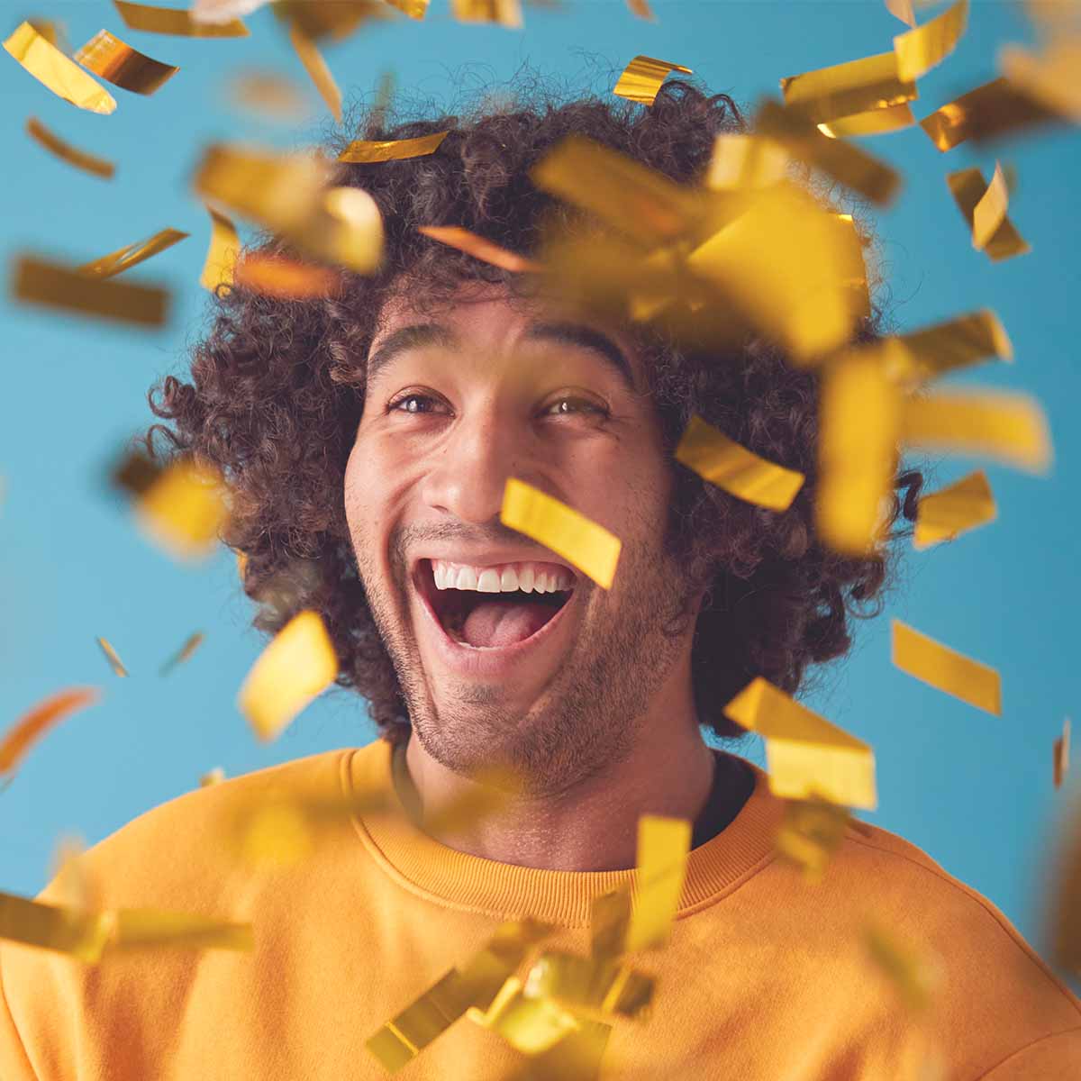 laughing man in yellow top with gold confetti